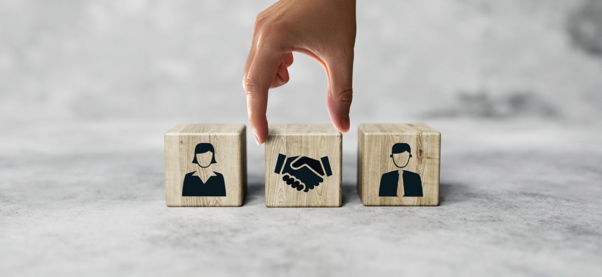The hand holds wooden wooden blocks with icons of a woman and a man and shaking hands in the act of consent.