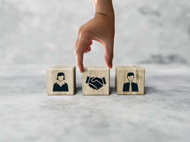 The hand holds wooden wooden blocks with icons of a woman and a man and shaking hands in the act of consent.